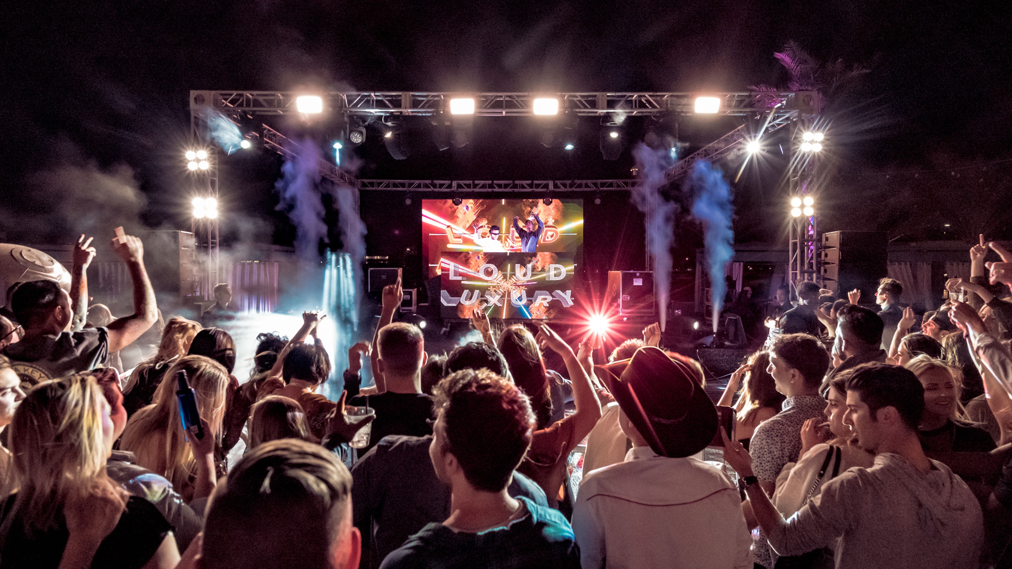 一名男子在弹奏电吉他，身穿绿色扎染衬衫，头戴白色渔夫帽，周围着一群热情的观众​。