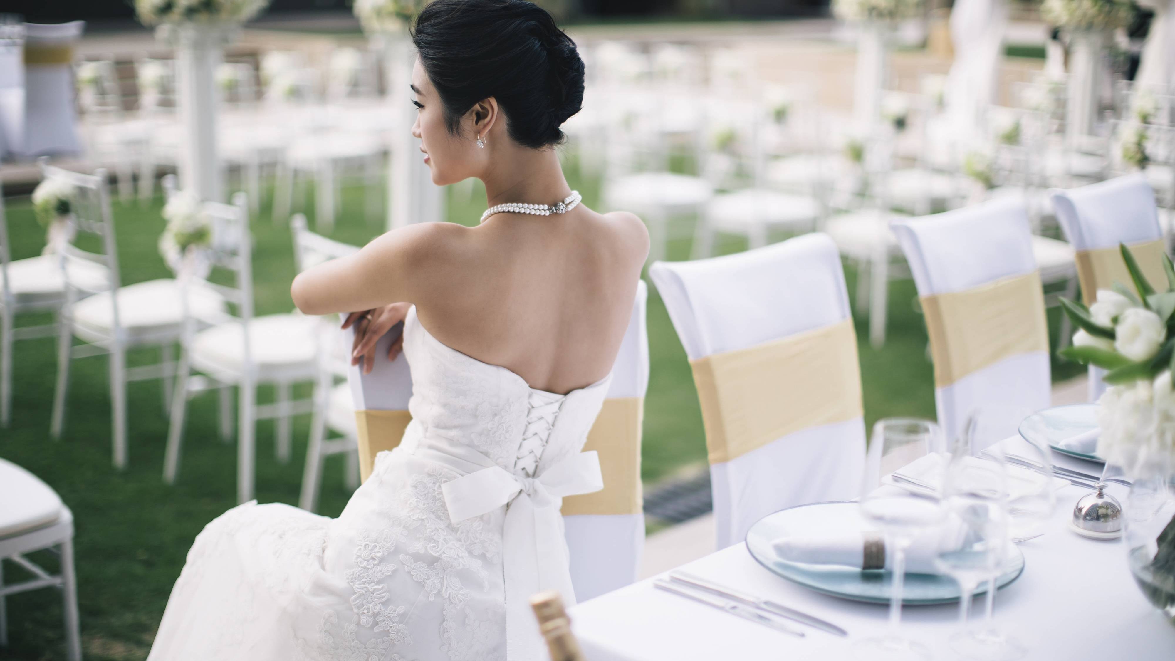 一个身穿白色婚纱的新娘坐在JW万豪酒店的草坪婚礼的椅子上
