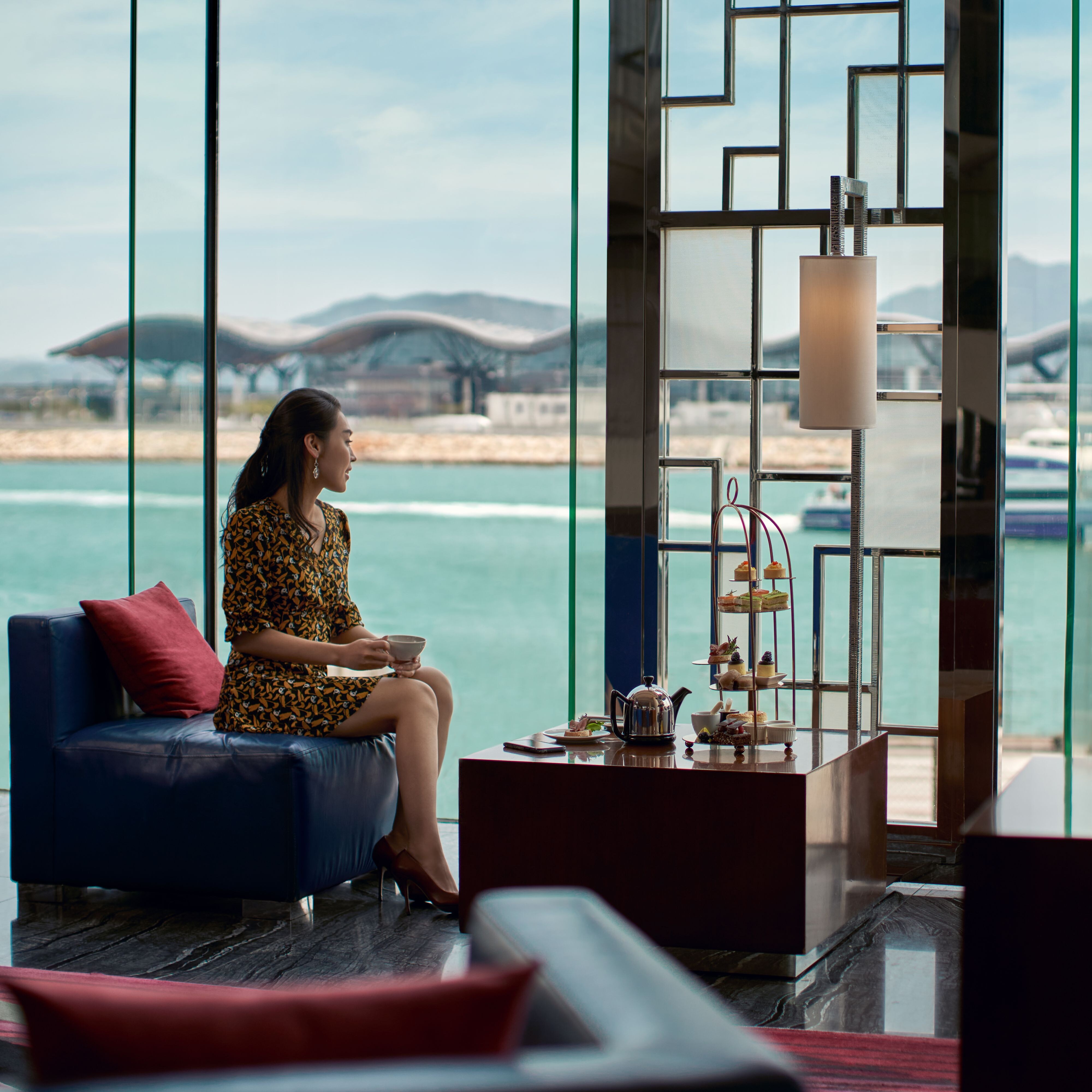 一位女性坐在沙发上享用下午茶并望向窗外