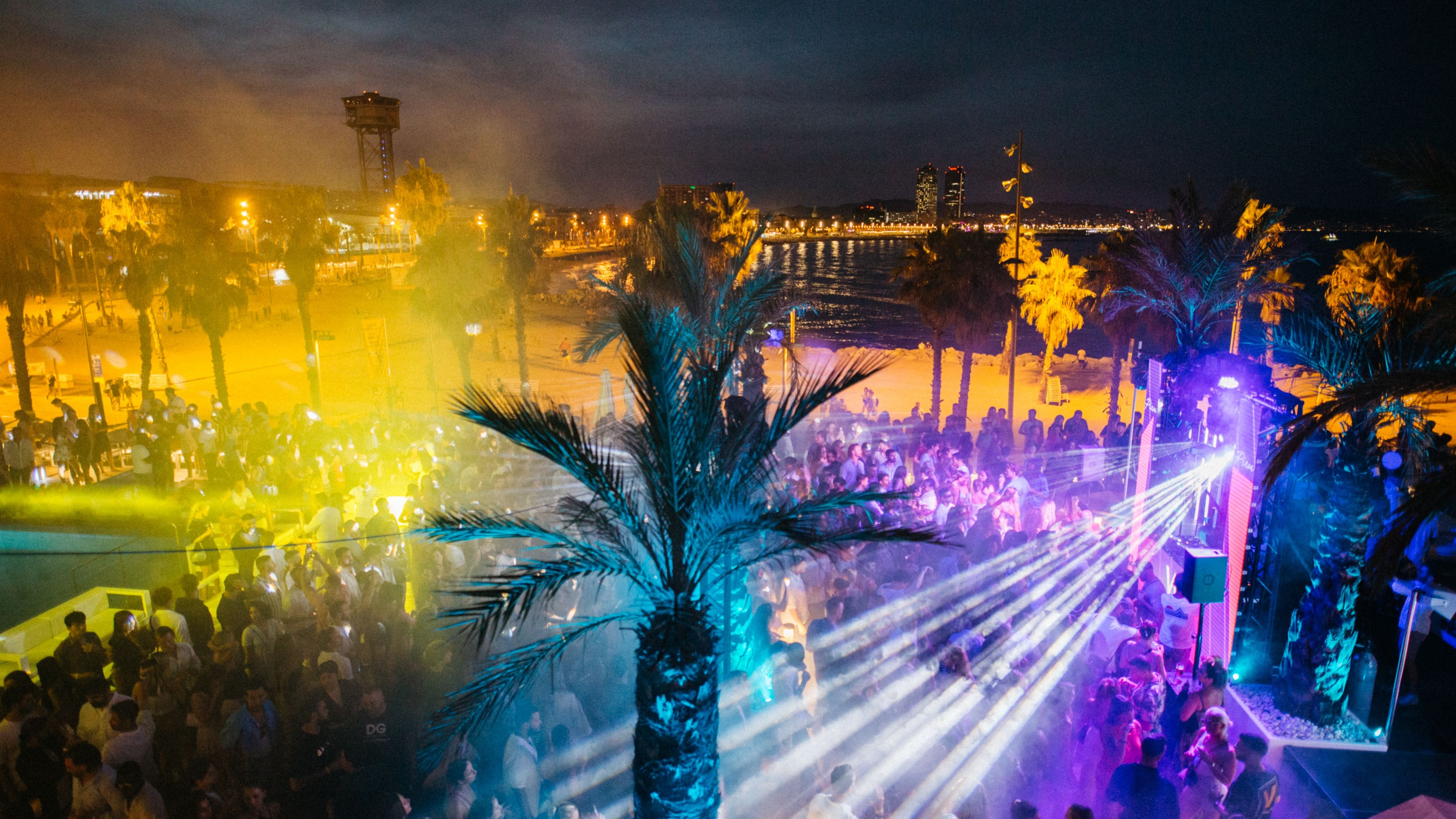 夜间活动中的一名 DJ 正在混音，DJ 台上方悬挂着超大粉色装饰物，营造出充满活力和身临其境的氛围。​