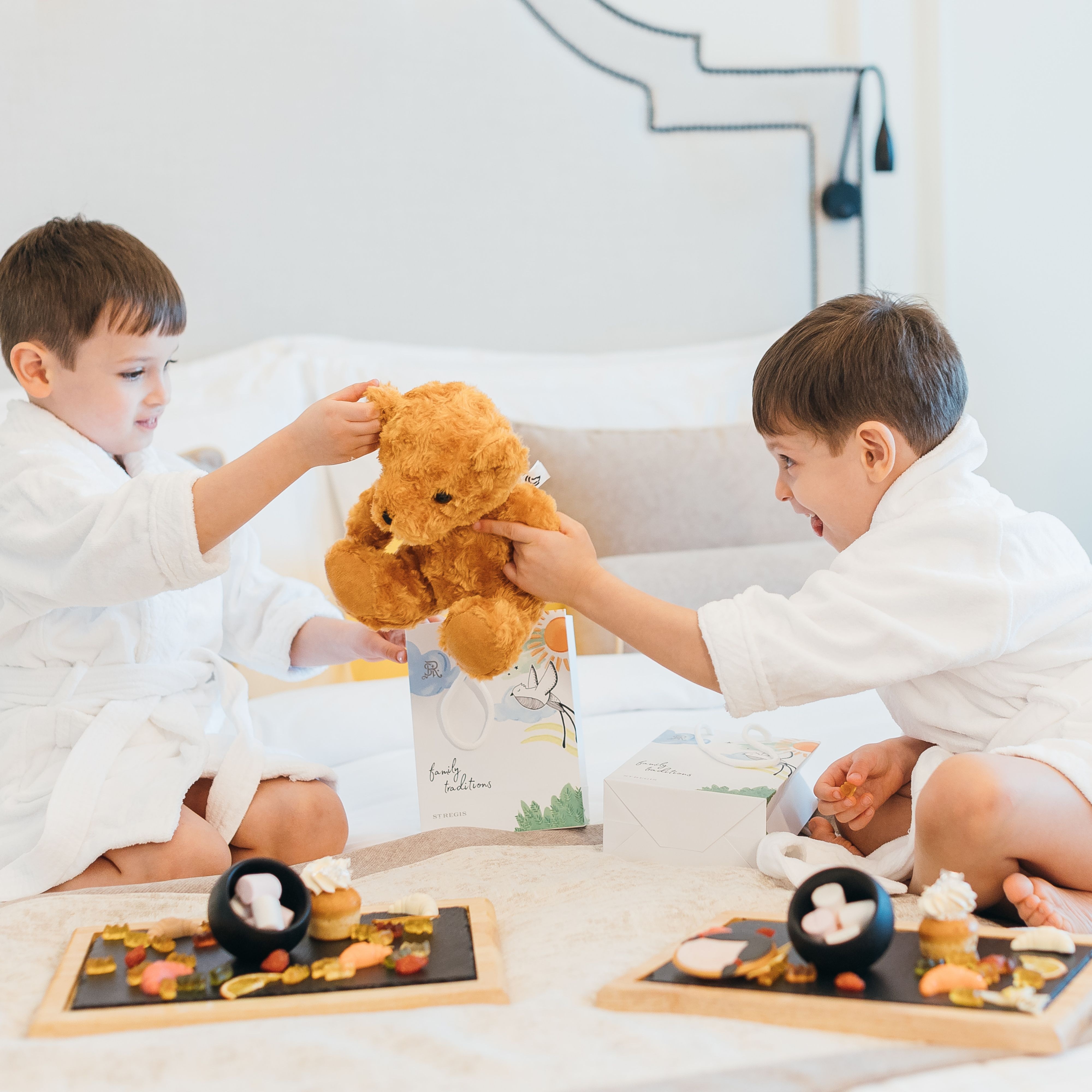 孩子们穿着浴袍，在床上抱着毛绒玩具玩耍