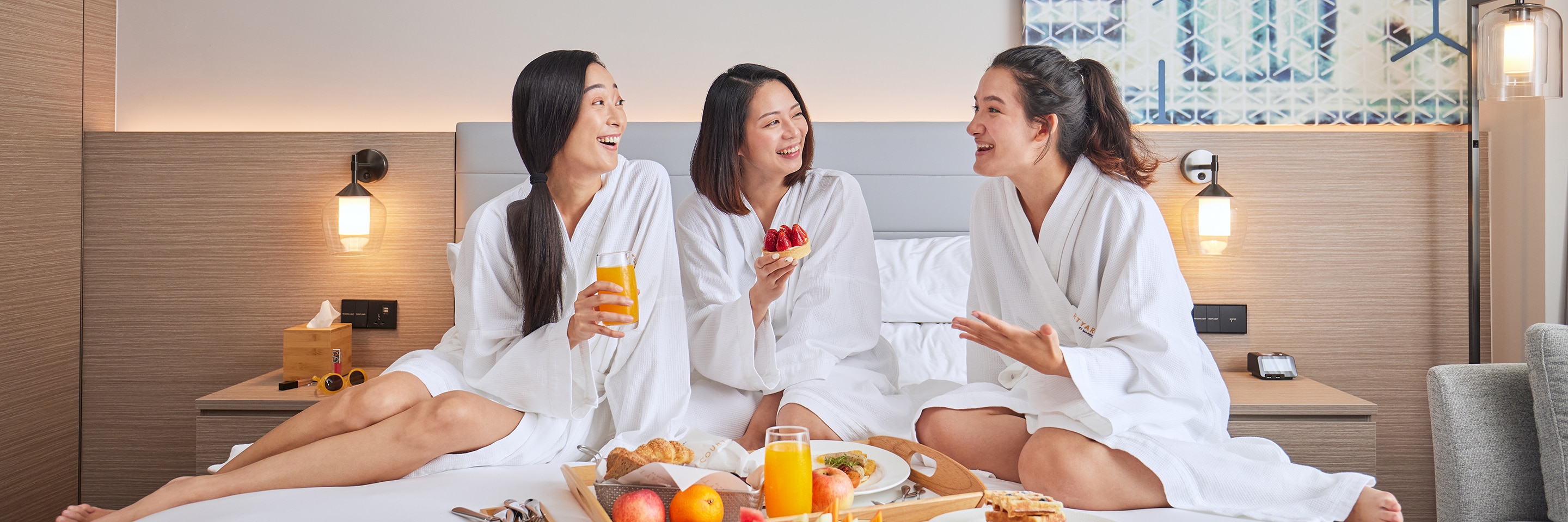 三个女生穿着浴袍在客床上享受早餐